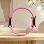 Pink circular resistance ring with two opposing padded handle assemblies and black mounts on a wooden table.