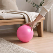 Pink ball on a wooden floor with a hand resting on the top.