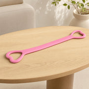 Long pink flexible strip with one rounded triangular handle opening at each end on a wooden table.