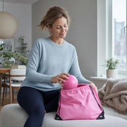 Woman seated at home holding a pink ball above an open pink drawstring bag.