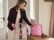Woman lifting a pink resistance ring beside a pink drawstring bag and face-down smartphone.