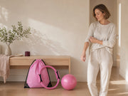 Woman preparing to move at home beside a pink drawstring bag, resistance ring and pink ball.